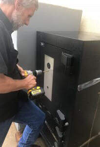 Man drilling a panel to the front of a black safe
